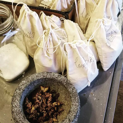 Many tea bags sit on a table next to a herb grinder.